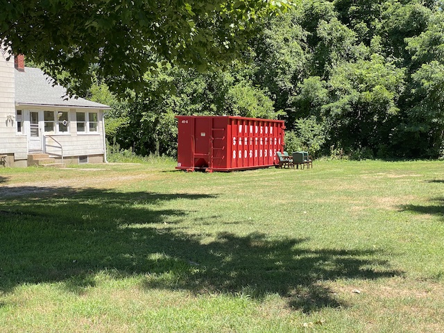 Merrigan's red roll-off dumpster next to farmhouse at 64 South Elm Street